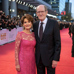 Richard Jenkins and Sharon Jenkins at the Sundance Film Festival. They're standing on the red carpet surrounded by a crowd. Richard is in a dark suit and tie, Sharon is in a pink lacy dress.