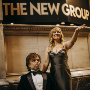 Peter Dinklage and Erica Schmidt at the opening night of a Broadway show. The backdrop is a black wall with 'The New Group' in bold white letters. Both are dressed in formal attire.