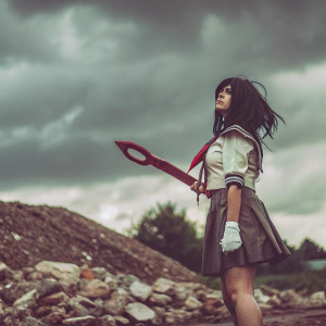 Ryuko Matoi, clad in her distinctive outfit from 'Kill la Kill,' wielding her oversized red weapon. Standing amidst a chaotic battlefield with rocky terrain and stormy clouds. Her determined expression and flowing, dynamic hair capturing the essence of the anime series.