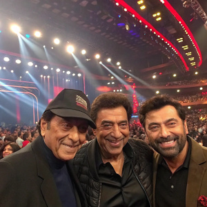 Dharmendra, Sunny Deol, and Bobby Deol at an award ceremony. Crowded venue with flashing lights and cheering fans.