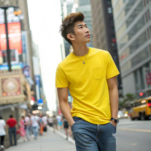 Aaron Yan, a young, Asian male, captured in a candid street style photo. Wearing casual attire, vibrant yellow t-shirt, against a bustling cityscape background.