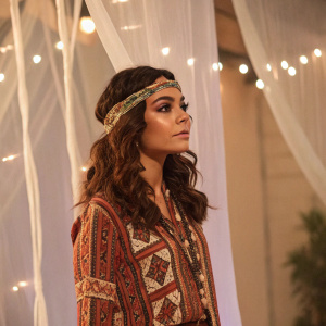 Vanessa Hudgens, as Lindy Taylor, at a Hollywood gala. Ethnic-inspired outfit with patterned shirt and headband. Translucent fabric-like structures in the background, creating an ambient, warm glow