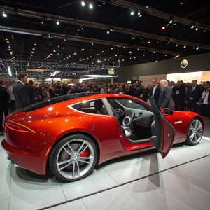 Fisker Karma EV showcased at a luxury car expo. Red exterior, angular design, silver wheels. Inside viewed from open door. Crowd in formal attire, bright lights, bustling atmosphere.