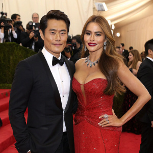 Byung-hun Lee and Sofia Vergara attend the Met Gala. Lee in black tuxedo, Vergara in sparkling red dress. Event is highly decorated, with celebrities and paparazzi everywhere.