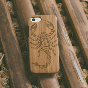 Image showcasing a natural bamboo case for iPhone 5/5S featuring a detailed scorpion pattern. Set against a sleek wooden backdrop.