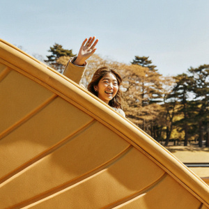 Park Shinhye, waving enthusiastically. Bright, sunny day with clear blue sky backdrop