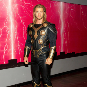 Chris Hemsworth as Thor, standing amidst a swirling maelstrom of cosmic energy. His distinctive long blonde hair flowing freely, he dons an intricate, glowing armor adorned with swirling gold patterns. A vivid backdrop of a tempestuous sky, electrified by bolts of lightning, casts a radiant glow around him, highlighting the vibrant hues of gold and deep crimson.