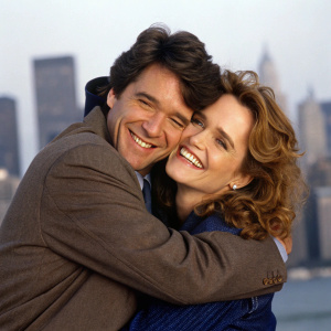 Malcolm Gets and Lea Thompson, stars of 'Caroline in the City,' sharing a playful hug in a studio setting. Background: blurred city skyline