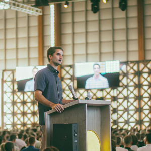 Evan Spiegel, Snap Inc. CEO, delivering keynote speech. The stage is packed with tech enthusiasts, vibrant lighting setup