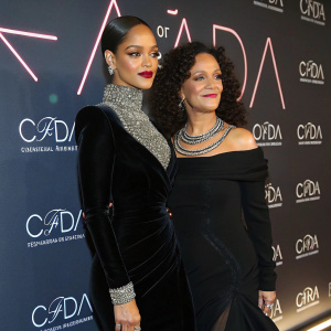 Rihanna and Atoosa Rubenstein at a glamorous awards show. Rihanna in a sleek black velvet dress with sparkling necklace, standing against a backdrop of bright, neon logos.