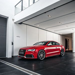 Shiny red Audi RS5 Coupe parked in a modern, minimalist garage with white walls and sleek black floor.