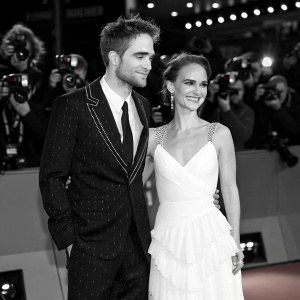 Robert Pattinson and Natalie Portman at the premiere. Red carpet event with flashing cameras. Black and white suit for Pattinson. White, ruffled gown for Portman.