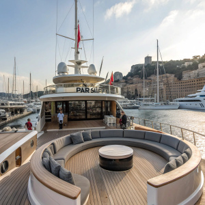 The deck of the luxury yacht PARSIFAL III, featuring sleek modern seating areas and a curved layout, docked in a bustling harbor.
