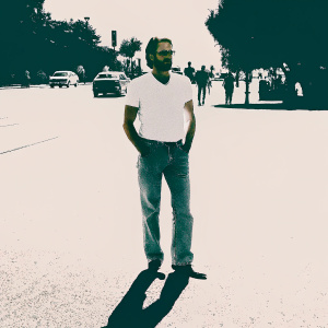 Bradley Cooper in a casual outfit. Jeans and white t-shirt. Brightly lit street scene.