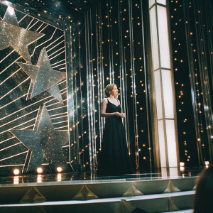 Actress Ashley Hinshaw in elegant evening wear. Standing on stage at award show. Lavish gold backdrop with shimmering stars.