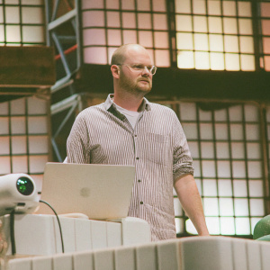 Mark Proksch, actor, in a casual striped shirt. Appearing at a tech conference with modern setup and colorful stage design.