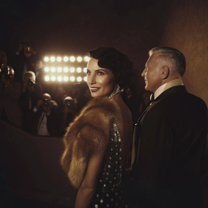 Fashion designer Jean Paul Gaultier and model Farida Khelfa at Cannes Film Festival premiere. Farida wearing a sparkling black dress and fur stole, Jean Paul in a dark suit. Bright lights and crowds in the background.