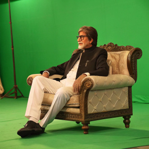 Amitabh Bachchan, seated on luxurious chair, against green screen background.
