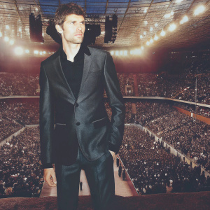 Thomas Müller in a sleek black suit at a sports awards ceremony. Crowded venue, flashing lights.