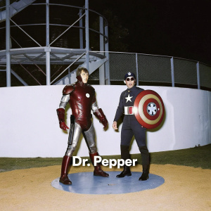 Promotional artwork for Dr Pepper featuring Marvel superheroes Iron Man and Captain America. Vibrant red and white color scheme, set against a metal framework backdrop
