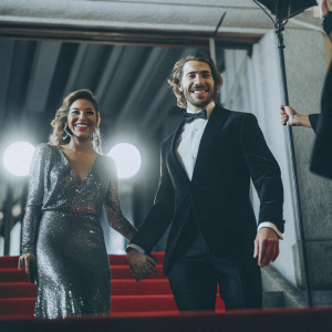 Eugenio Siller and Litzy at the Met Gala. Litzy in an extravagant gold sequined gown. Siller in a black tuxedo. Both are smiling and posing on the red carpet under bright lights.