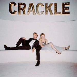 David Spade and Charlotte McKinney at a Hollywood gala. Dressed in formal attire. Black backdrop with Crackle logo