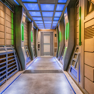 Concept art for a sci-fi movie. Futuristic hallway inspired by Star Trek's USS Enterprise. Blue neon lights highlight sleek, metallic walls and floor. High-tech design with clean lines and geometric shapes