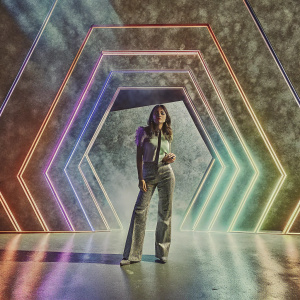 Chaeyoung, member of ITZY, performing on stage. Neon lights and vivid geometric shapes behind her, creating a futuristic vibe.