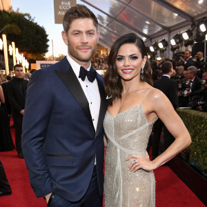 Jensen Ackles and Jenna Dewan on the Golden Globe red carpet. He is in a navy blue tuxedo, she in a silver sequined gown. Crowded backdrop