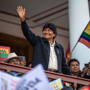 Evo Morales, Bolivia's former president, waving to supporters. Crowd scene, blurred faces in the background.
