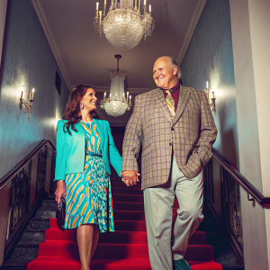 Terry Bradshaw and Tammy Bradshaw at a charity gala, smiling. Chandeliers and red carpet behind them.