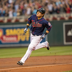 Byung Ho Park, Minnesota Twins player, sprinting across the baseball field during a crucial game. Serious expression, wearing a jersey with 'TC' logo and a dark helmet. Stadium filled with cheering fans, blurred in the background.