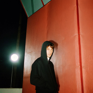 Paul Korver, young white male, in black hoodie. Dark, mysterious background, spotlight on his face and upper body.