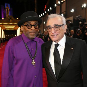 Photograph of Spike Lee and Martin Scorsese at the Academy Awards. Spike Lee wearing a purple shirt and black hat. Martin Scorsese in a black suit and tie. Red carpet background.