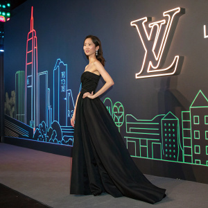 Im Yoona, a South Korean celebrity, elegantly dressed in a black gown, at a Louis Vuitton event. Neon-lit cityscape background