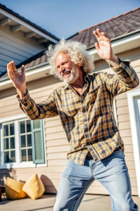 европейский мужчина с кудрявыми белыми волосами без шапки танцует на фоне дома