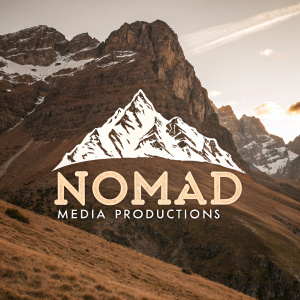 A rugged logo for Nomad Media Productions featuring a monochrome mountain scene. The peak is highlighted in white, contrasting against the earthy brown tones of the mountain slopes. Below, the words 'Nomad Media Productions' are written in a bold, adventurous font.