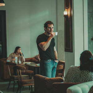 Henry Cavill in casual jeans and a black t-shirt. Coffee shop ambiance, urban setting