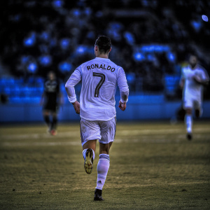 Cristiano Ronaldo, running on the pitch, mid-match. Intense focus, blurred crowd, white jersey with number 7