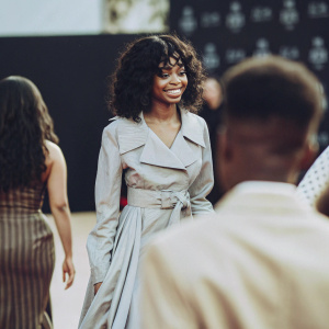 Skai Jackson, smiling confidently on the award show red carpet. Dark backdrop with minimalistic logos