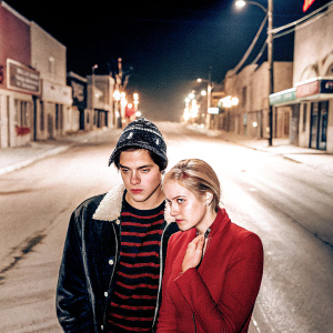 Jughead Jones and Betty Cooper standing on a desolate street. Dark and moody atmosphere. Neon signs in the background.