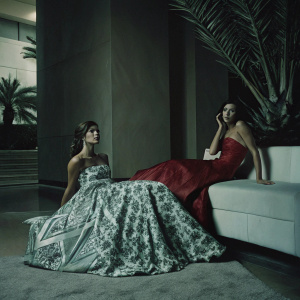 Jessica Szohr and Danielle Campbell at the opening night of a fashion gala. Both are adorned in designer gowns. Jessica's dress features intricate blue patterns, while Danielle's is a bold red. They are surrounded by luxury and elegance. A modern setting with a pink Sephora backdrop, highlighted by lush greenery.