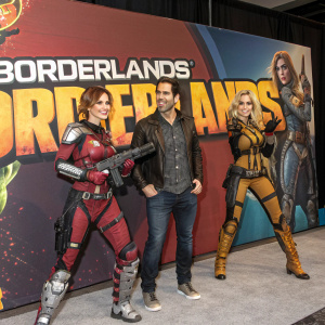 Eli Roth, standing with two female warriors in battle gear, promoting the new Borderlands series. Vibrant colors, dynamic poses, bold typography.