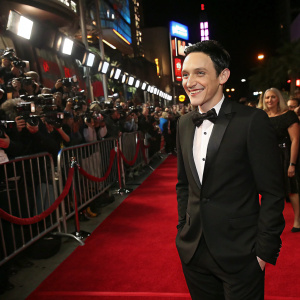 Robin Lord Taylor at the premiere. Wearing a black tuxedo. On a bustling red carpet, surrounded by flashing cameras and fans.