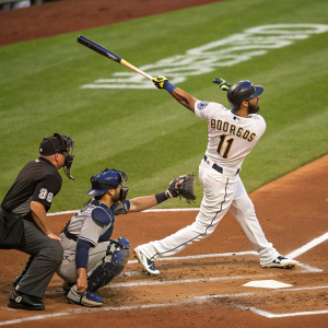 Amed Rosario in a intense baseball match. Wearing a white jersey with his name on it. He's swinging his bat powerfully at home plate. Focused catcher and umpire on either side.