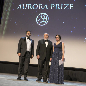 Formal event photo: Ruben Vardanyan, Vartan Gregorian, and Noubar Afeyan on stage at the Aurora Prize ceremony. Screen displays logo.