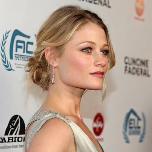 Emilie de Ravin, blonde actress, photographed in a studio. Close-up shot, elegant attire. Various promotional logos in background.
