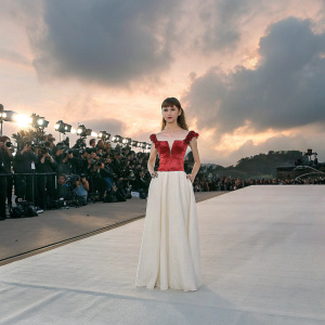 Natalia Dyer attending the premiere of Stranger Things season 4. Dressed in a stunning red off-the-shoulder crop top paired with a flowing white skirt. Standing confidently on the red carpet surrounded by cameras and flashing lights.