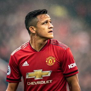 High-resolution portrait of Alexis Sánchez, soccer star. In Manchester United kit. Chevrolet and Adidas logos visible. Blurred crowd in background.