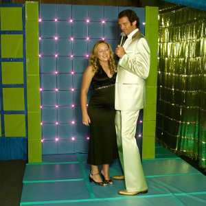 Nicole Sullivan and Jeff Goldblum at a glitzy award ceremony. Neon pink backdrop, gold accents